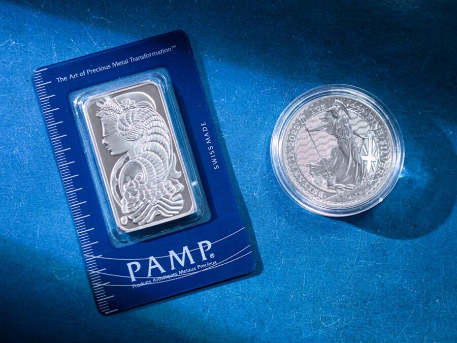 Close-up of a silver coin and a PAMP bar on a blue textured background emphasizing wealth.